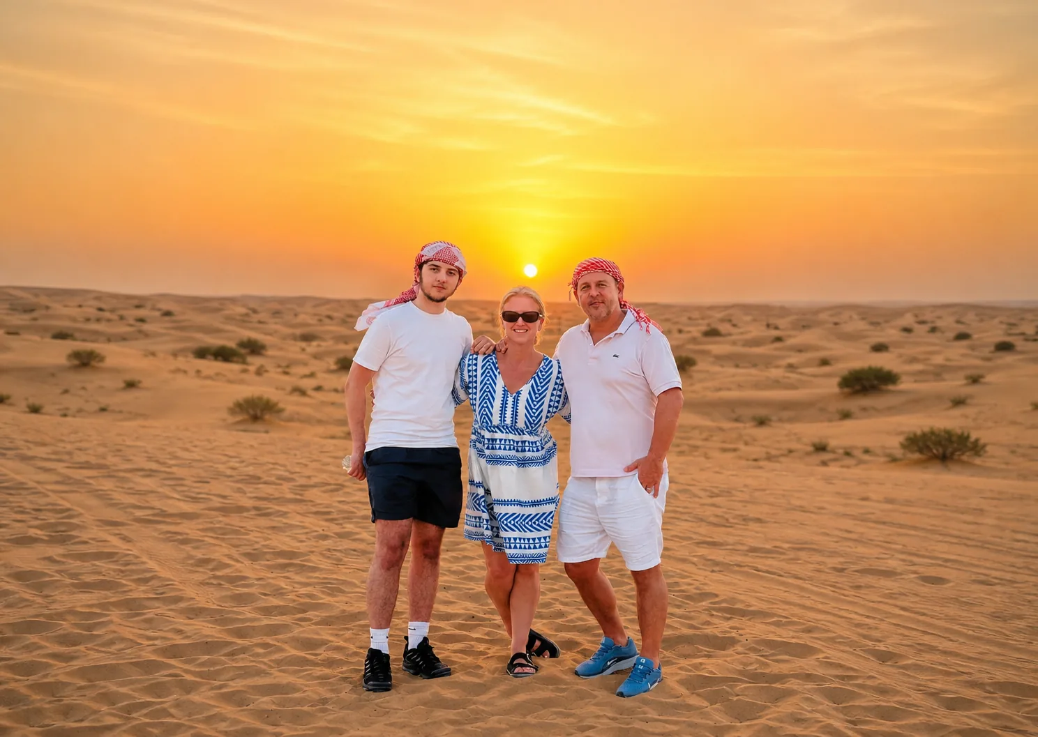 Family of three in keffiyehs posing on Abu Dhabi dunes at sunset during a Luxury Desert Safari
